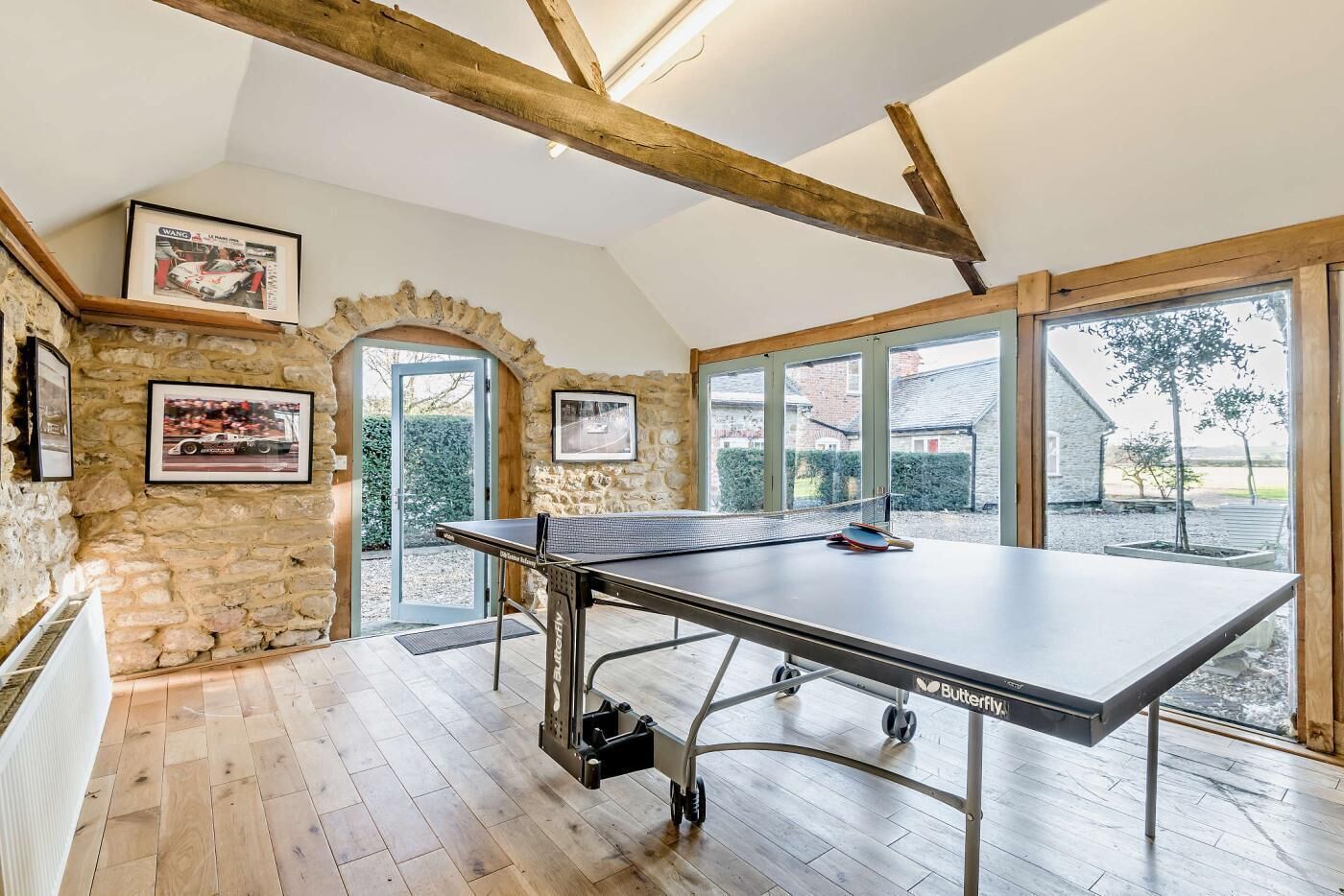 Une table de ping-pong dans une pièce aux murs de pierre, aux poutres en bois et aux grandes fenêtres.