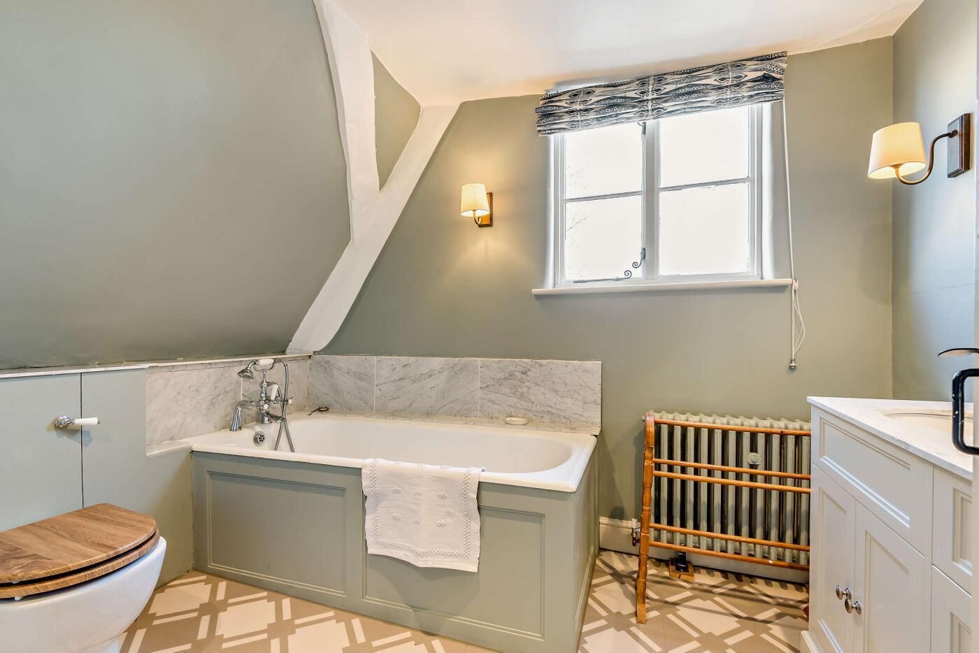 A bathroom with a freestanding bathtub, a toilet, a vanity with a mirror, and a radiator.