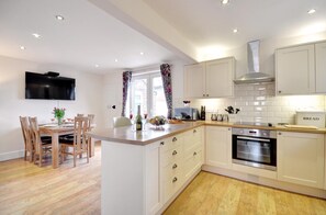 A modern kitchen with white cabinets, a central island, and a dining area with wooden chairs. - 3 Bed in Whitby (oc-w416) (Whitby)