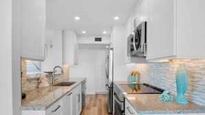 Una cocina moderna con armarios blancos, encimera de granito y salpicadero con azulejos azules.