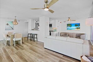 Ein geräumiger Wohnbereich mit weißem Sofa, Esstisch mit Stühlen und einer Küche im Hintergrund.