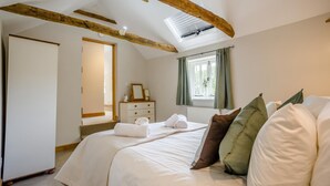 Un dormitorio con cama, cómoda, ventana con cortinas y vigas de madera a la vista.