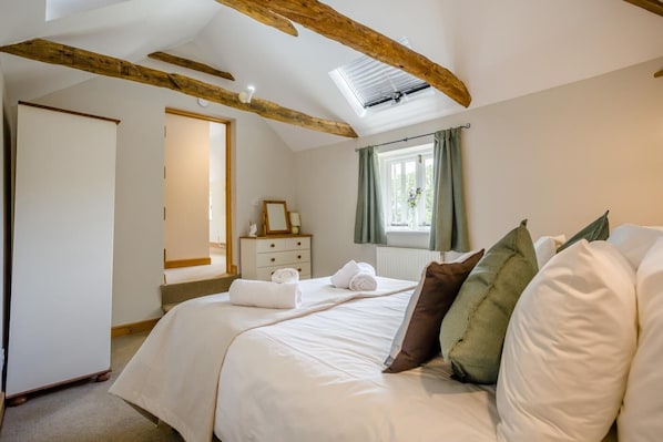 A bedroom with a bed, a dresser, a window with curtains, and exposed wooden beams.