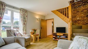 Una sala de estar con televisor, escalera de madera y vista al exterior.