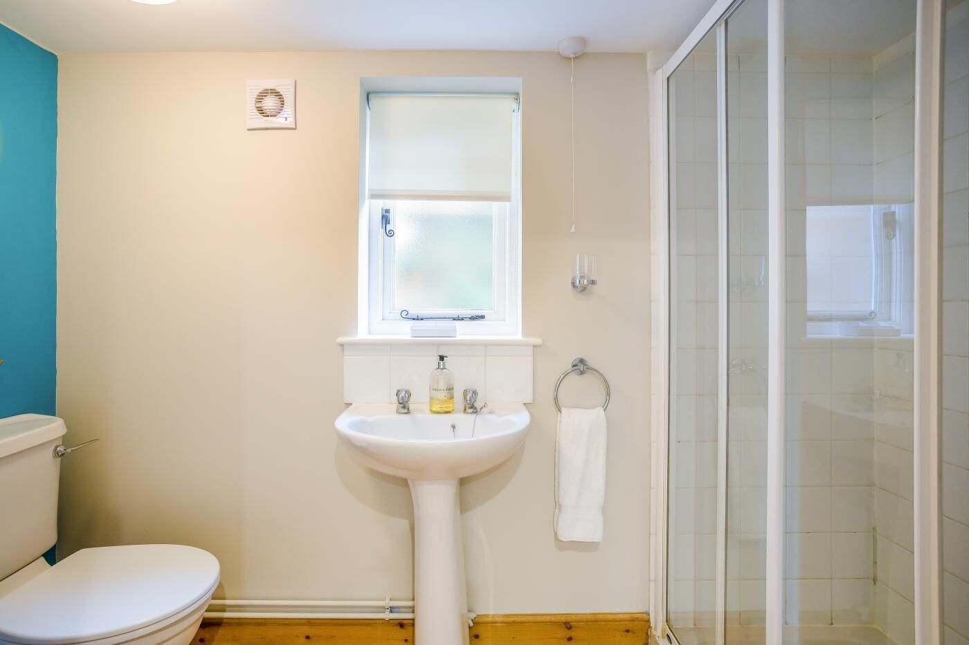 A bathroom with a white sink, a toilet, a window, and a glass shower enclosure.