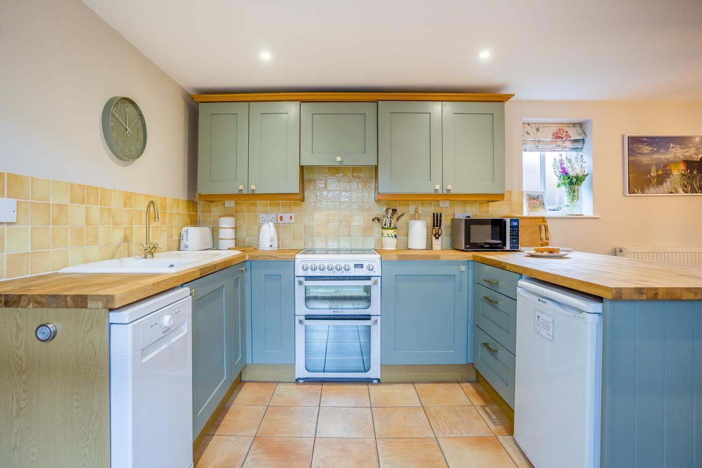 A kitchen with light blue cabinets, a white stove, a microwave, and a sink.