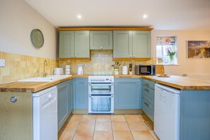 A kitchen with light blue cabinets, a white stove, a microwave, and a sink.