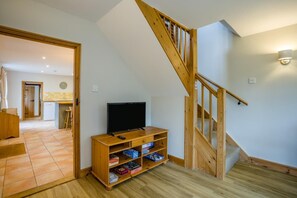 A room with a wooden TV stand, a staircase, and a kitchen in the background.