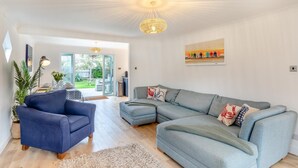 A spacious living room with a large grey sectional sofa, a blue armchair, and a chandelier. - 4 Bed in Freshwater (oc-s33684) (Freshwater)