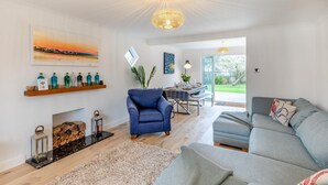 A modern living room with a blue armchair, grey sofa, and a dining area with a table and chairs. There is a fireplace with a mantel and a hanging light fixture. - 4 Bed in Freshwater (oc-s33684) (Freshwater)