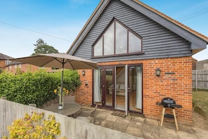 A house with a brick exterior, a large glass door, and a patio with a table and umbrella. - 1 Bed in Snape (oc-fcf) (Snape)