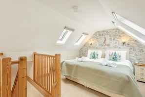 A bedroom with a sloped ceiling, skylights, a bed with a green bedspread, and a wall with a tree pattern.