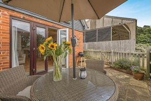 A patio with wicker furniture, a glass table, and a vase of sunflowers.