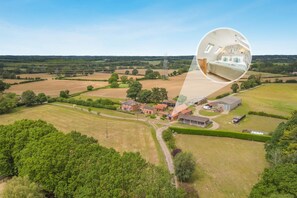 An aerial view of a rural property with fields, a farmhouse, and a detached house.