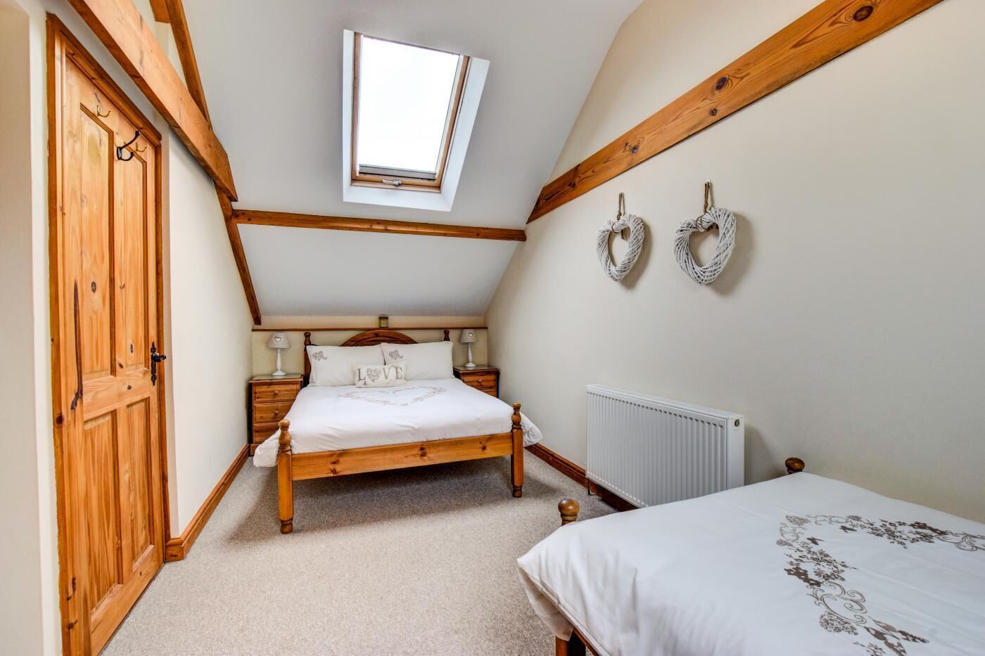 Een slaapkamer met een schuine kap, een dakraam, een houten bed, een nachtkastje, een radiator en een tweede bed.