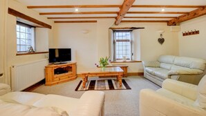 Un salon chaleureux avec un plafond en bois, une télévision, un canapé, une table basse et une fenêtre avec des rideaux.