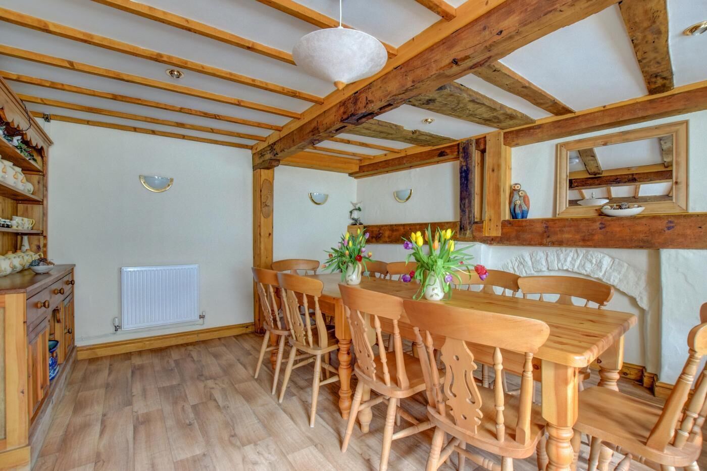 A dining area with a wooden table and chairs, a white radiator, and wooden beams on the ceiling.