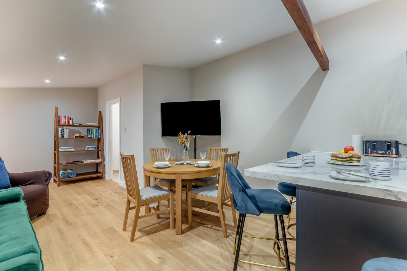 A dining area with a round table, chairs, a bookshelf, and a flat-screen TV.