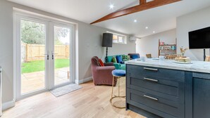 A modern kitchen with a large island, a dining area with a sofa, and a TV mounted on the wall. - 2 Bed in Latton (oc-c34099) (Latton)