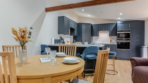 A modern kitchen with dark cabinets, a central island, and a dining area with a round wooden table and chairs. - 2 Bed in Latton (oc-c34099) (Latton)