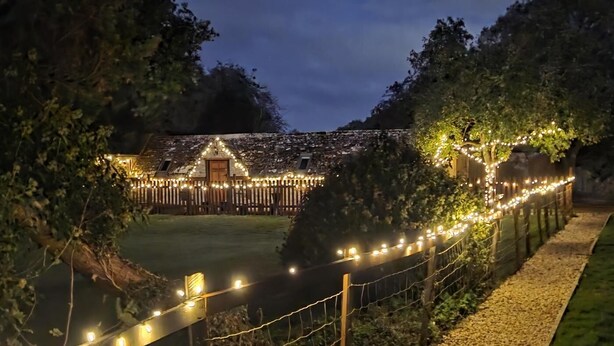 A fenced outdoor area with string lights, a wooden structure, and trees. - 2 Bed in Latton (oc-c34099) (Latton)