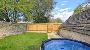 A backyard with a hot tub, a wooden fence, and a stone wall. - 2 Bed in Latton (oc-c34099) (Latton)