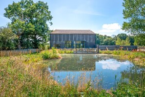 A modern building with a metal exterior, a glass entrance, and a pond in the foreground. - 5 Bed in Briston (oc-2304) (Briston)
