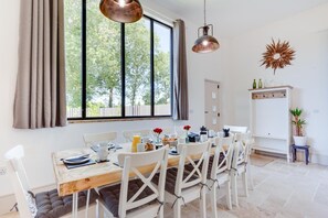 A dining area with a wooden table, white chairs, and a large window with curtains. - 5 Bed in Briston (oc-2304) (Briston)