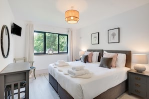 Ein Hotelzimmer mit Bett, Nachttischen, einem Schreibtisch, einem Sessel, einem Fenster mit Aussicht und einem Fernseher.