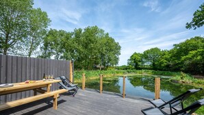 Un terrazzo in legno con tavolo e sedie, affacciato su un'acqua calma e una vegetazione lussureggiante.