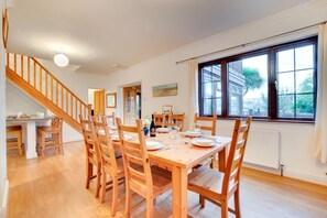 A dining area with a wooden table set for four, a staircase, and a window with a view of greenery. - 3 Bed in Saundersfoot (oc-pw9096) (Saundersfoot)