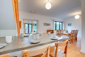 A spacious dining area with a granite countertop, white chairs, and a wooden dining table. - 3 Bed in Saundersfoot (oc-pw9096) (Saundersfoot)