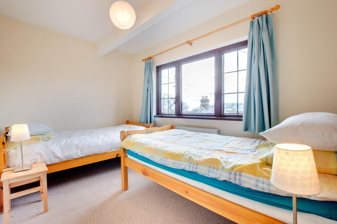 A room with two wooden beds, a small table, and a window with curtains.
