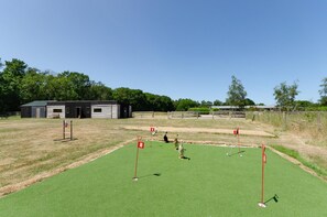 Een golfbaan met een putting green, een clubhuis en een omheind gebied met bomen.