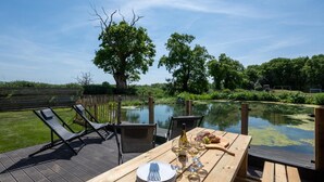 A wooden deck with a table set for dining, overlooking a pond and surrounded by trees. - 5 Bed in Briston (oc-2305) (Briston)