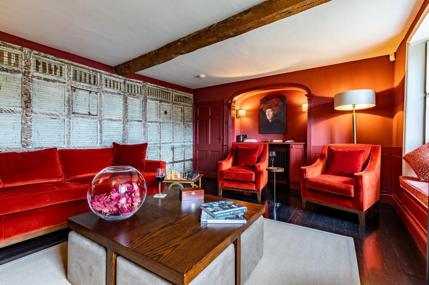 Una habitación con un sofá rojo, dos sillones rojos, una mesa de centro de madera y un florero de vidrio con flores.