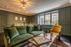 A room with a green sofa, a yellow armchair, a coffee table with a board game, and a large window with a view of greenery. - 5 Bed in Padstow (oc-p00595) (Padstow)