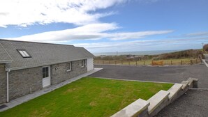 A stone building with a sloped roof, a grassy area in front, and a paved driveway leading to a wooden fence. - 3 Bed in Llanon (oc-porth) (Llan-non)