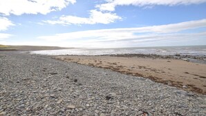 A pebbled beach with a rocky foreground and a sandy area. - 3 Bed in Llanon (oc-porth) (Llan-non)