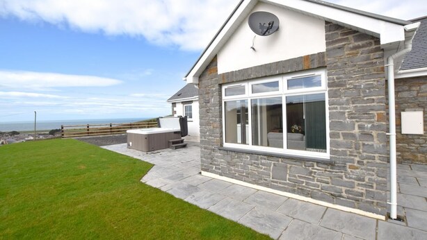 A house with stone exterior, a hot tub, and a view of the sea. - 3 Bed in Llanon (oc-porth) (Llan-non)