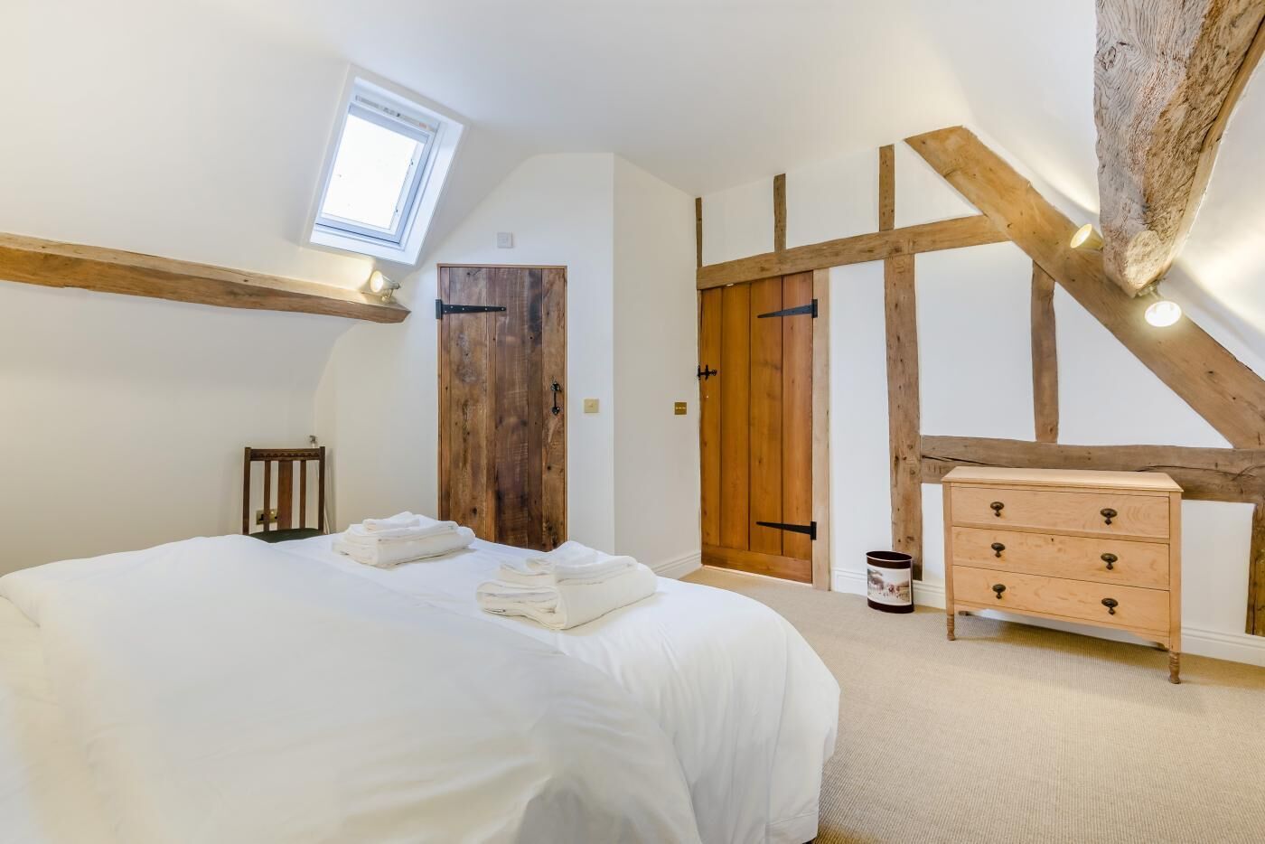 A bedroom with a large bed, wooden beams, a wooden wardrobe, and a skylight.