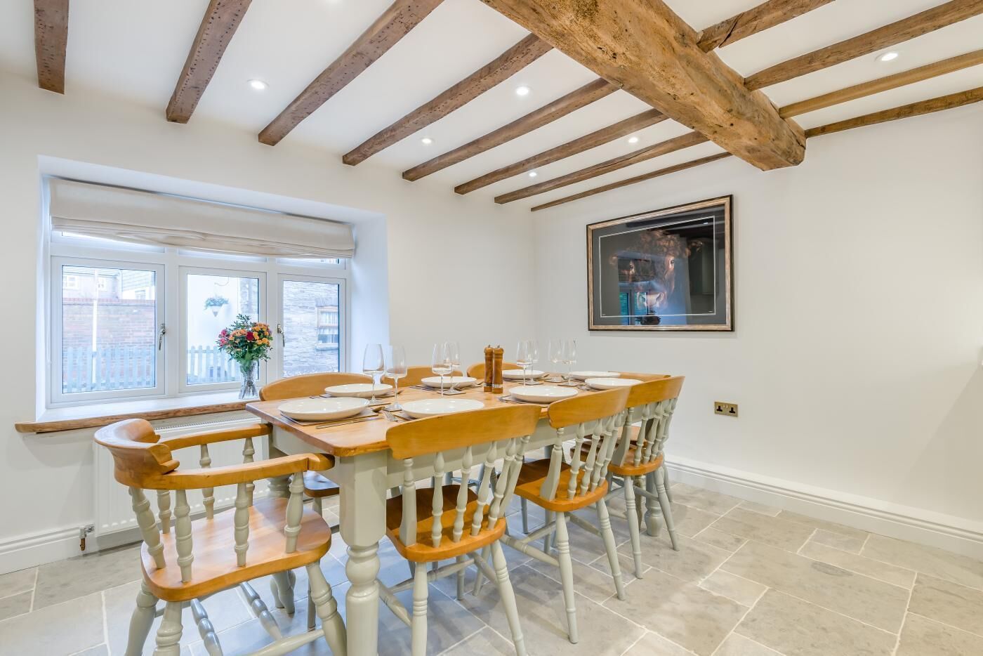 Un comedor con una mesa de madera dispuesta para seis personas, sillas blancas y un ventanal con vistas al exterior.