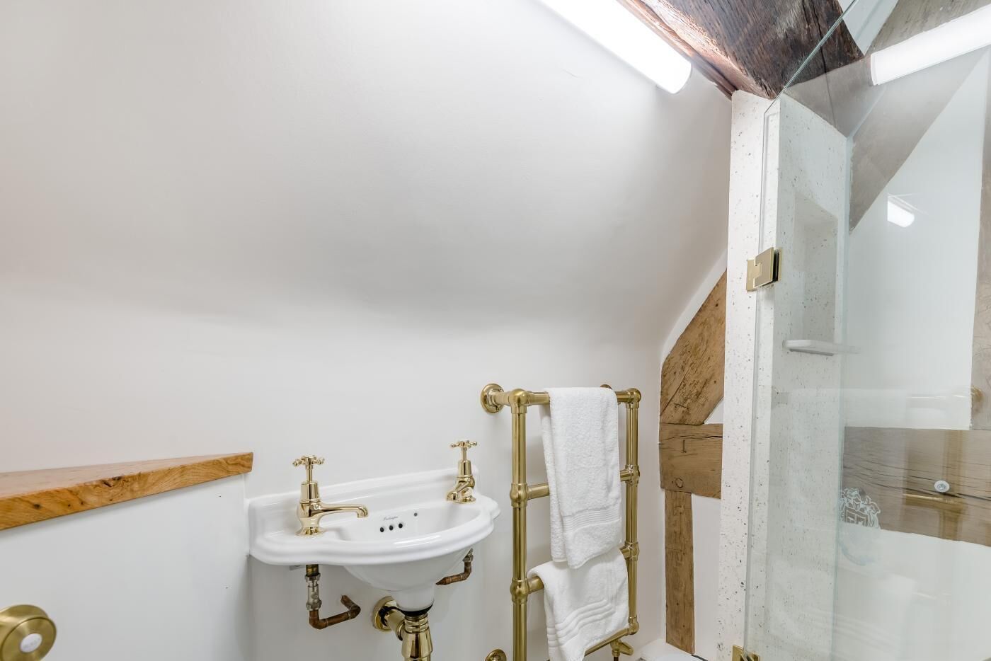 A bathroom with a white sink, gold fixtures, and a glass shower enclosure.