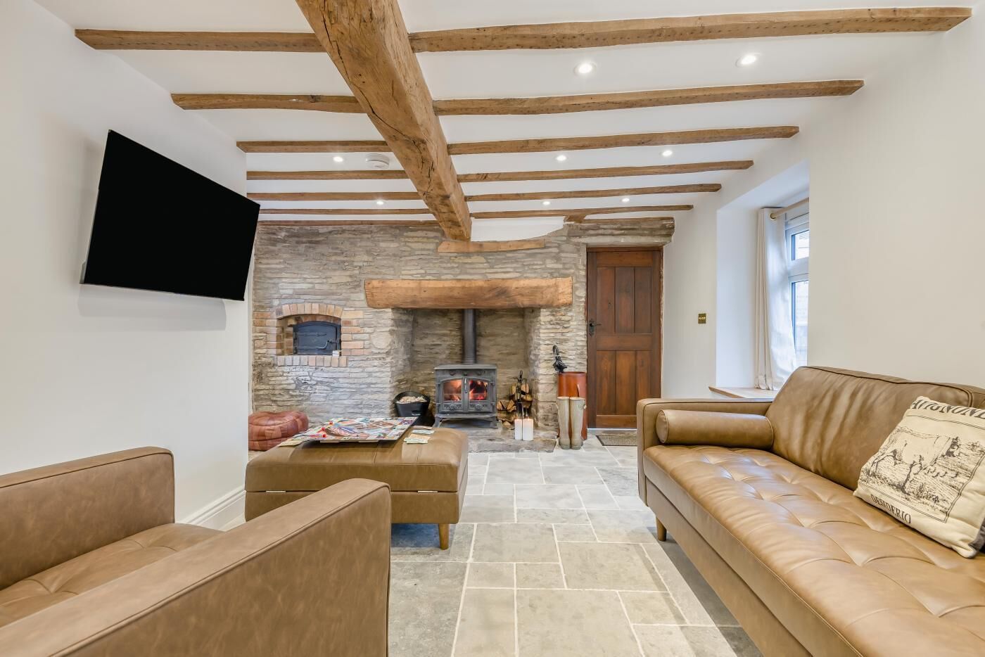 A cozy living room with a stone fireplace, leather sofas, and a flat-screen TV mounted on the wall.