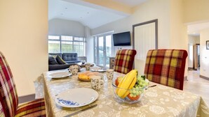 A dining area with a table set for four, chairs, a bowl of fruit, and a sofa in the background. - 2 Bed in Llanon (oc-porth1) (Llan-non)