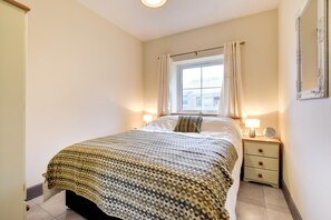 Un dormitorio con cama, mesitas de noche, una ventana con cortinas y un espejo en la pared.