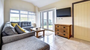 A spacious living room with a grey sofa, a wooden cabinet, and a television mounted on the wall. - 2 Bed in Llanon (oc-porth1) (Llan-non)