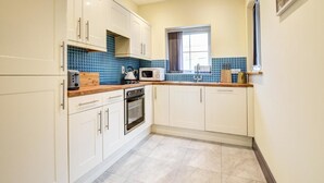 A compact kitchen with white cabinets, a microwave, a toaster, and a kettle. - 2 Bed in Llanon (oc-porth1) (Llan-non)