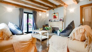A cozy living room with wooden beams, a fireplace, and a large window with curtains. - 4 Bed in Tenby (oc-pw9264) (Tenby)