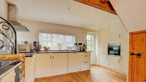 A kitchen with wooden flooring, white cabinets, a built-in oven, and a window with blinds. - 3 Bed in Llanrhychwyn (oc-wag577) (Llanrhychwyn)